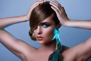 Model in stylish image with sleek hair covering one eye and feather earring photo