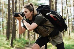 Hiker taking photos using modern mirrorless camera in green forest