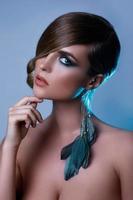 Model in stylish image with sleek hair covering one eye and feather earring photo