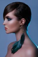 Model in stylish image with sleek hair covering one eye and feather earring photo