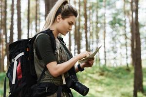 Female hiker with big backpack using map for orienteering in the forest photo