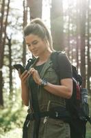 Female hiker is using smartphone for navigation in green forest photo