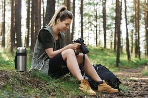 Hiker sitting with modern mirrorless camera in green forest photo