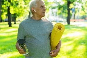 Active elderly man with a exercise mat and bottle of water in green city park photo