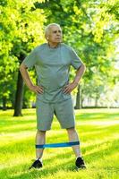 Active elderly man exercising with a rubber resistance band in green city park photo