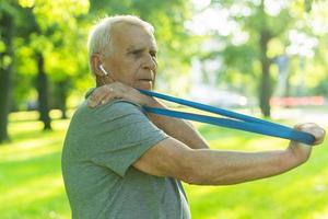 Active elderly man exercising with a rubber resistance band in green city park photo
