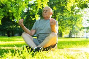 Elderly man meditating during his yoga workout in green city park photo