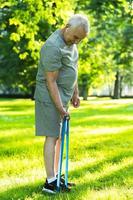 Active elderly man exercising with a rubber resistance band in green city park photo