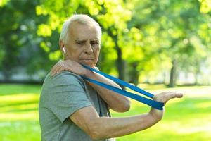 Active elderly man exercising with a rubber resistance band in green city park photo