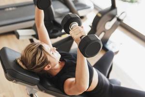 Young athletic woman doing bench press using dumbbells photo