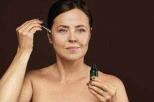 Beautiful middle aged woman holding bottle with cosmetic oil or serum for her skin photo