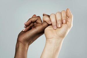 A pinky promise gesture between African and Caucasian women. Closeup of palms on gray background. photo