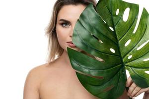 hermosa mujer caucásica con una piel suave sosteniendo una hoja tropical verde foto