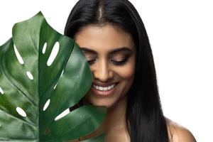 hermosa mujer india con una piel suave sosteniendo una hoja tropical verde foto