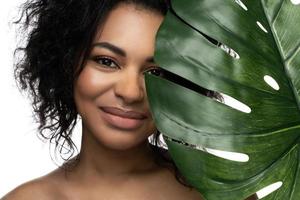 Beautiful black woman with a smooth skin holding green tropical leaf photo