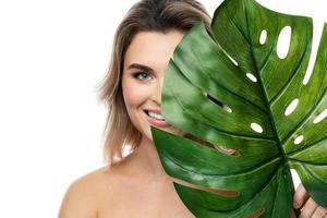bella mujer con una piel suave sosteniendo una hoja tropical verde foto