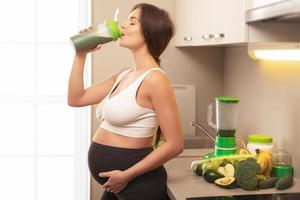 Happy pregnant woman drinking green protein cocktail photo
