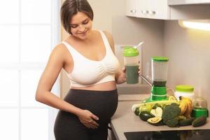 mujer embarazada sosteniendo un agitador con un cóctel de proteína verde foto