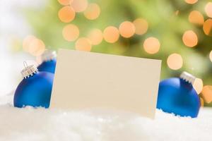 adornos navideños azules detrás de una tarjeta blanquecina en blanco foto