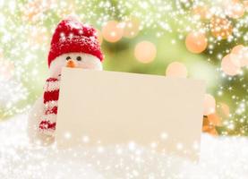 Snowman with Blank White Card Over Abstract Snow and LIght photo