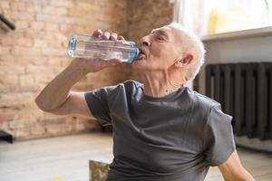 anciano activo bebiendo agua después de hacer ejercicio en casa foto