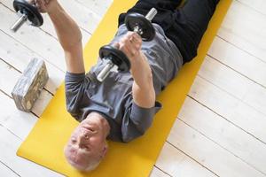 Elderly man exercising with a dumbbells during his workout in home gym photo