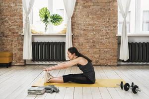 Elderly woman sitting and stretching on a yellow mat during her fitness workout at home photo
