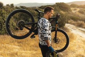 Professional downhill rider carrying his bicycle on shoulder photo