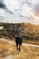 Professional downhill rider carrying his bicycle on shoulder photo