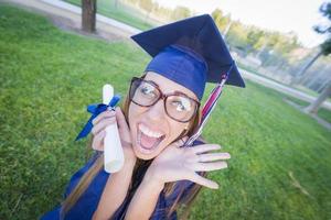 Expressive Young Woman Holding Diploma in Cap and Gown photo