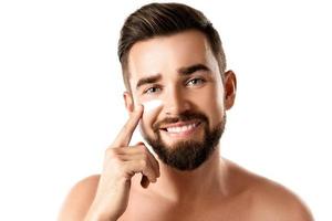 Young man is applying moisturizing and anti aging cream on his face photo