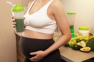 Pregnant woman holding shaker with a green protein cocktail photo