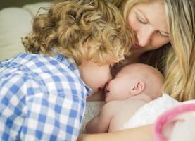 Young Mother Holds Newborn Baby Girl as Brother Looks On photo