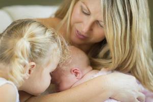 Young Mother Holds Newborn Baby Girl with Young Sister photo