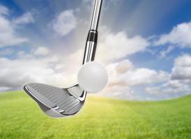 Chrome Golf Club Wedge Iron Hitting Golf Ball Against Grass and Blue Sky Background photo