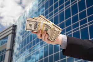 Male Hand Holding Stack of Cash with Corporate Building photo