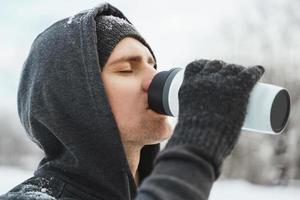 Man athlete drinking from the thermal mug during snowy winter day photo