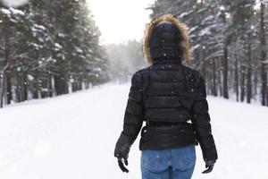 mujer con chaqueta con capucha caminando en el parque durante el frío día de invierno foto