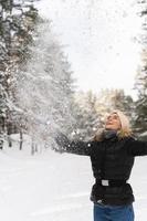 Cheerful woman throwing snow into the air during cold winter day photo