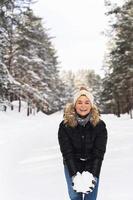 mujer joven sosteniendo un montón de nieve en sus manos durante su caminata en el parque de invierno foto