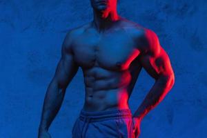 Bodybuilder is posing in the colorful neon light photo