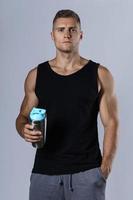 Man wearing blank black tank top is drinking protein or other supplement from a metal shaker photo