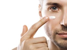 Men's beauty. Young man is applying moisturizing and anti aging cream on his face photo