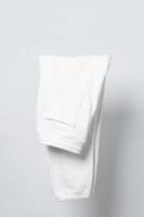 pantalones de chándal blancos en blanco colgando de una percha contra un fondo gris foto