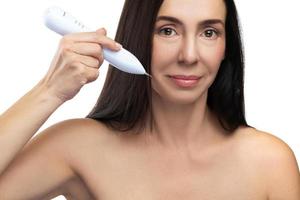 Middle aged woman using plasma pen for a non-invasive skin rejuvenation. photo