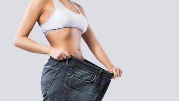 mujer que muestra el resultado después de la pérdida de peso usando jeans viejos foto