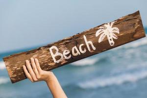 mano femenina y cartel de madera antiguo con playa de letras foto