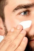 Young man is applying moisturizing and anti aging cream on his face photo