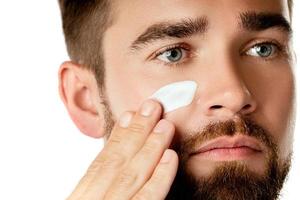 Young man is applying moisturizing and anti aging cream on his face photo