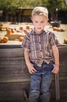 adorable niño parado contra un viejo vagón de madera en un huerto de calabazas en un entorno rural. foto